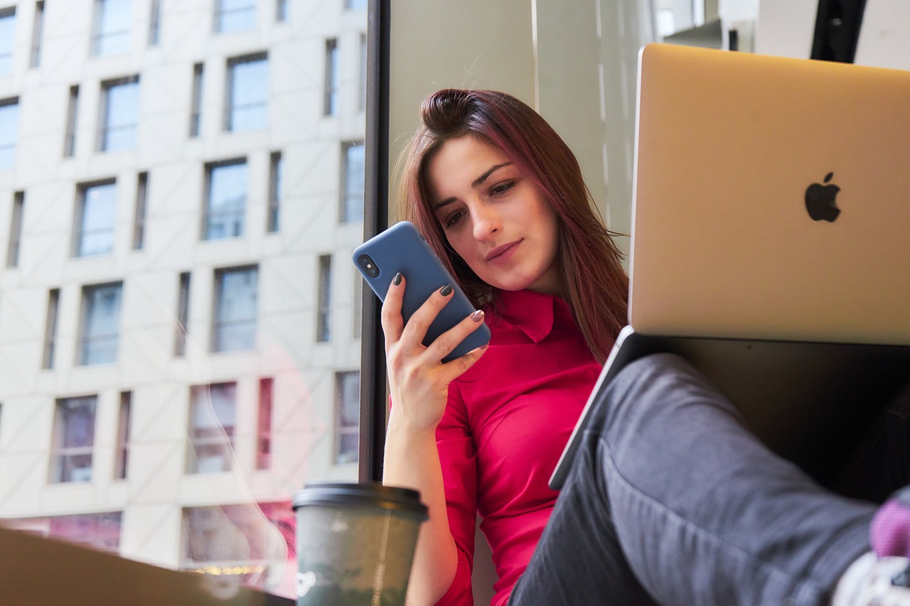 Femme avec son portable et son laptop au bord d'une fenête